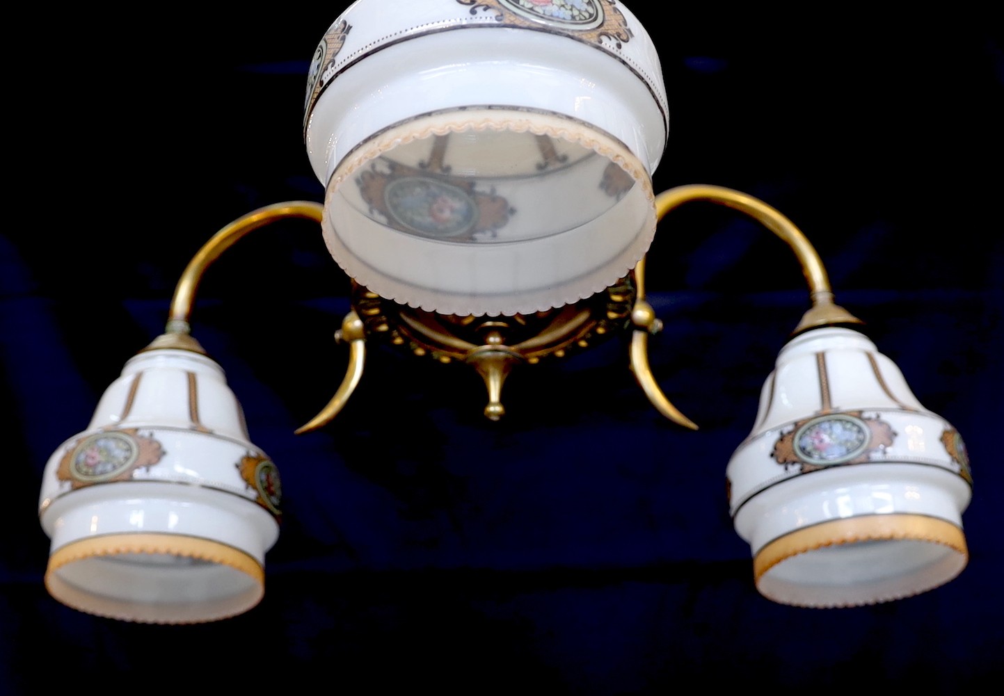An early 20th century English lacquered brass light fitting with three stencilled opaque glass shades, height 65cm. width 50cm